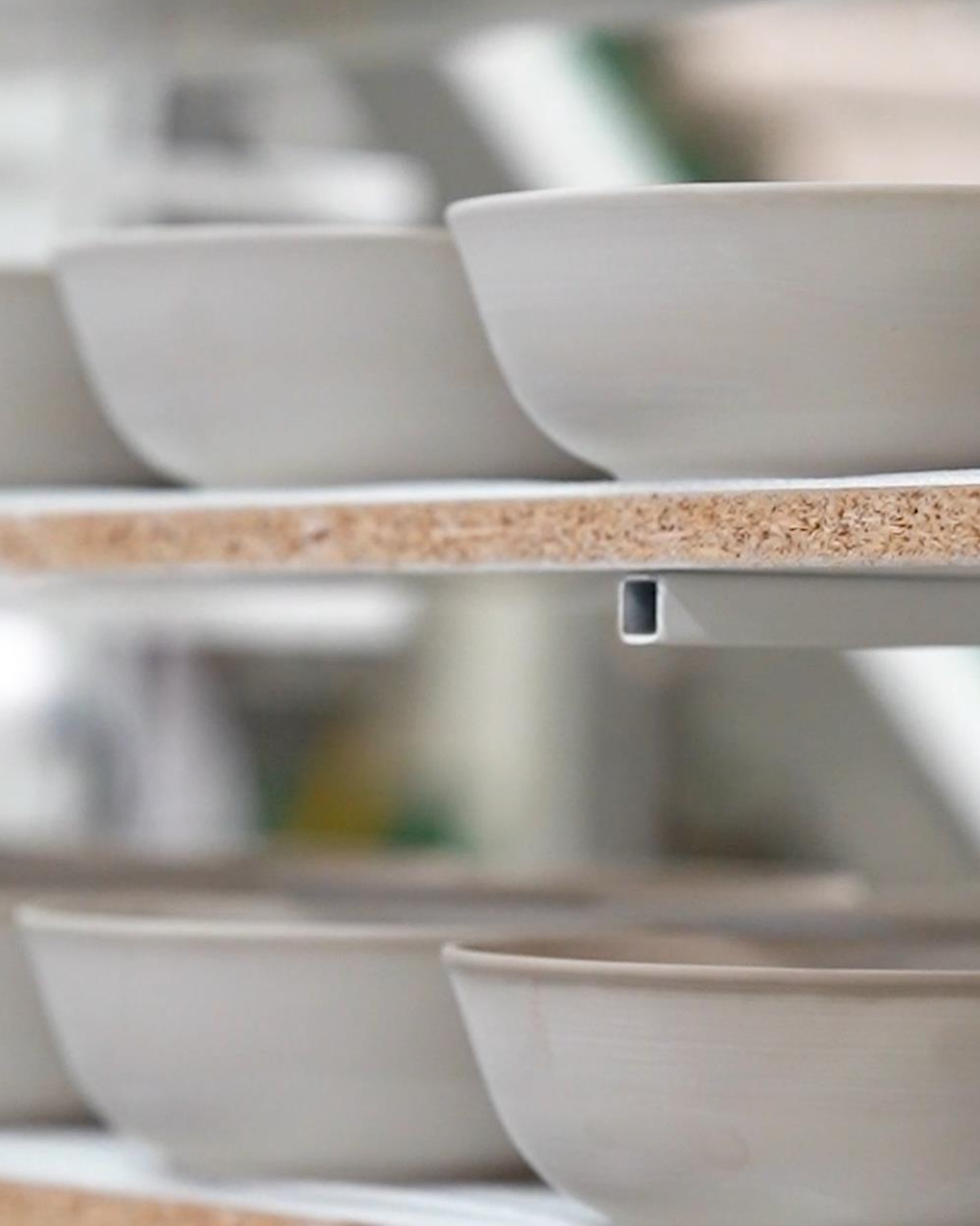 Unfinished ceramic bowls drying on shelves during Hamkke Home’s Portugal manufacturing process, showing raw clay pieces before glazing.