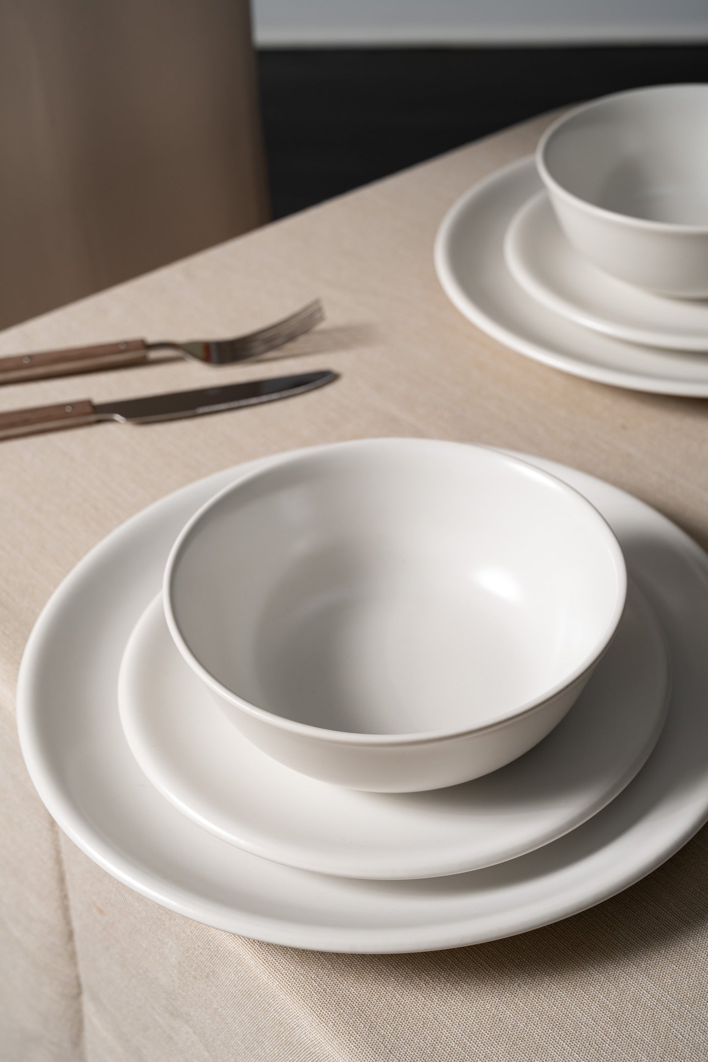 Bone-colored ceramic bowl and plates from Hamkke Home styled on a neutral linen tablecloth with wooden-handled flatware.