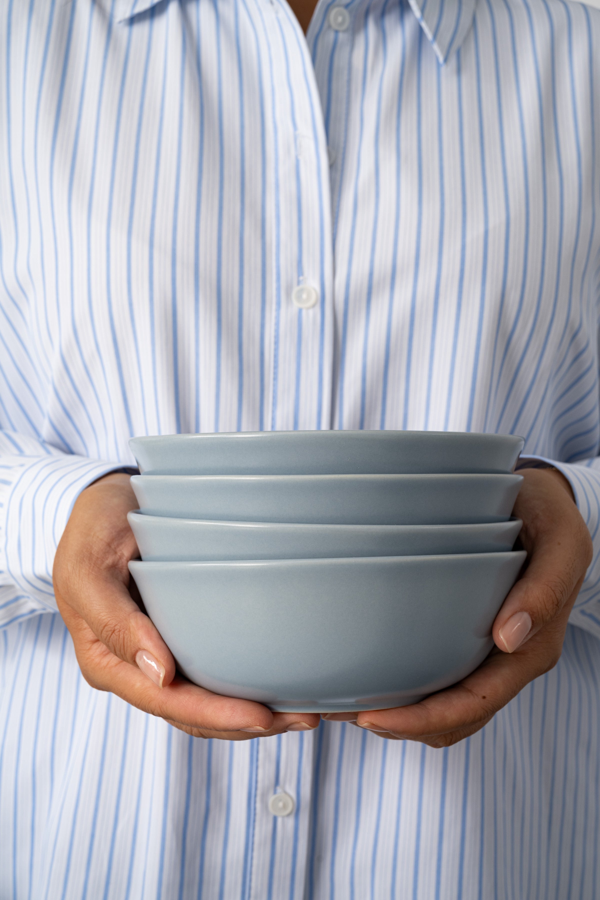 Person holding a stack of Wave blue ceramic bowls from Hamkke Home, showcasing the hand-finished stoneware design.