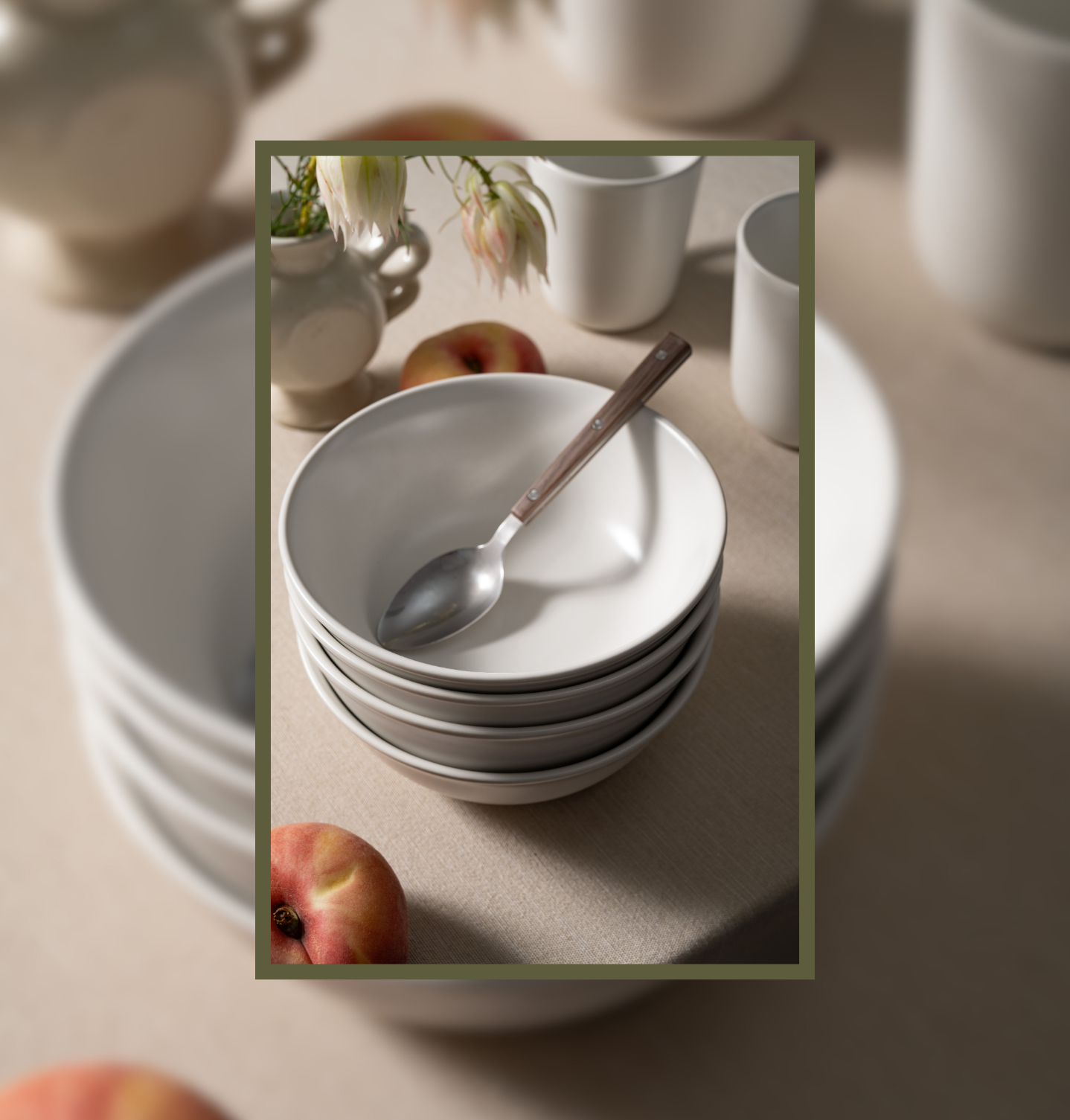 Stacked Bone-colored ceramic bowls from Hamkke Home with a spoon, styled alongside peaches and ceramic vessels on a neutral table setting.