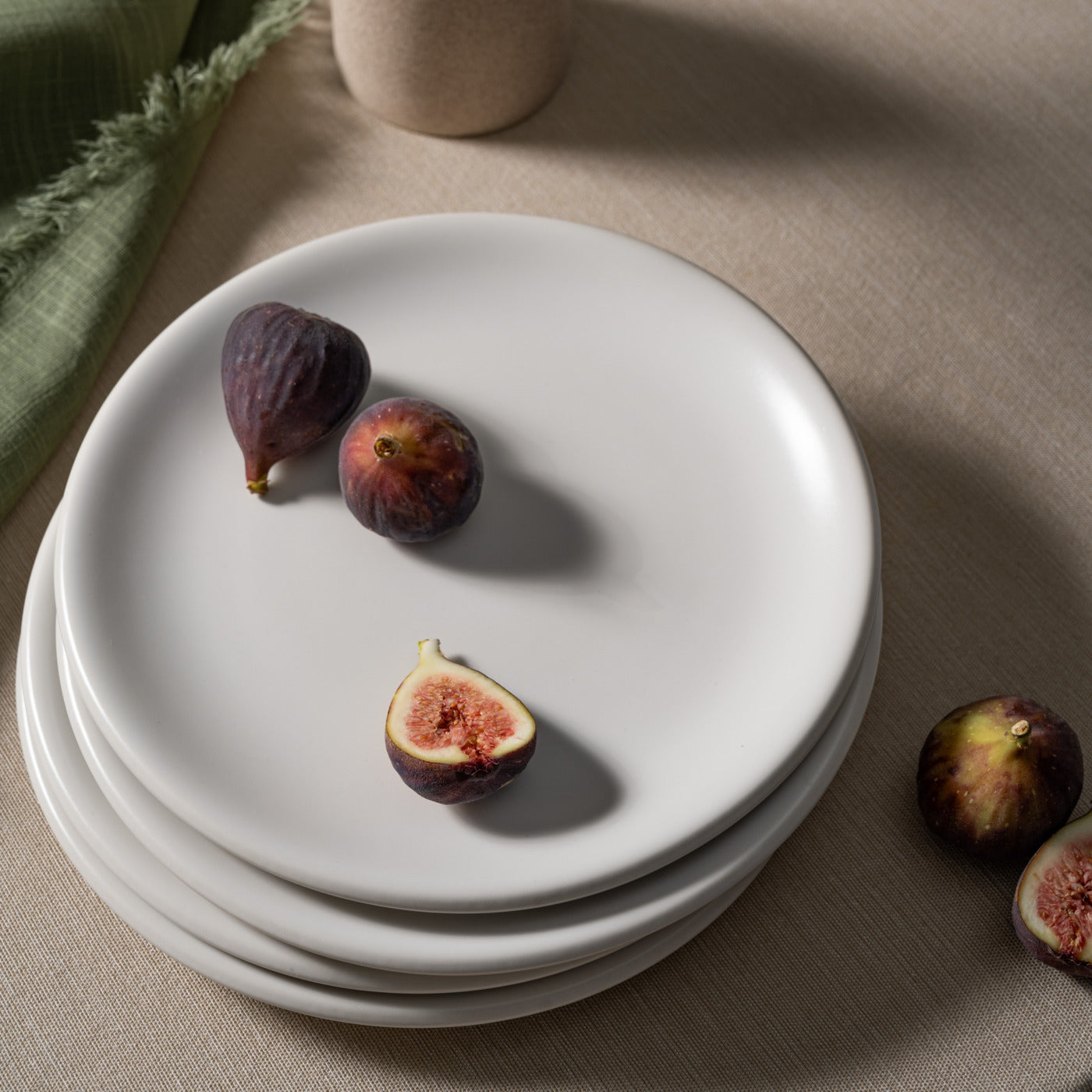 Bone-colored ceramic plates from Hamkke Home stacked on a linen tablecloth, styled with fresh figs for a minimal food photography look.